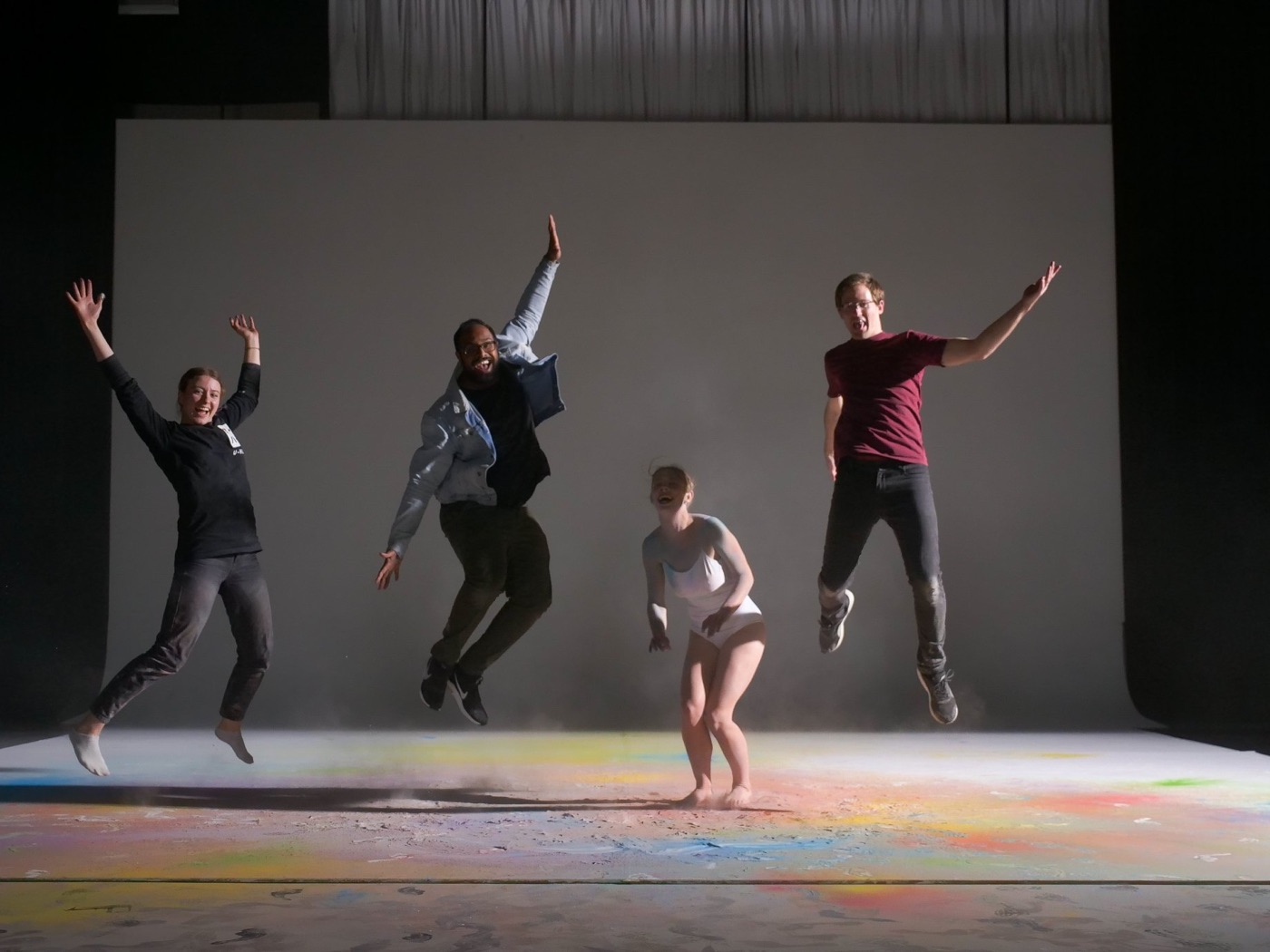 Dance company mid-leap on a dark stage