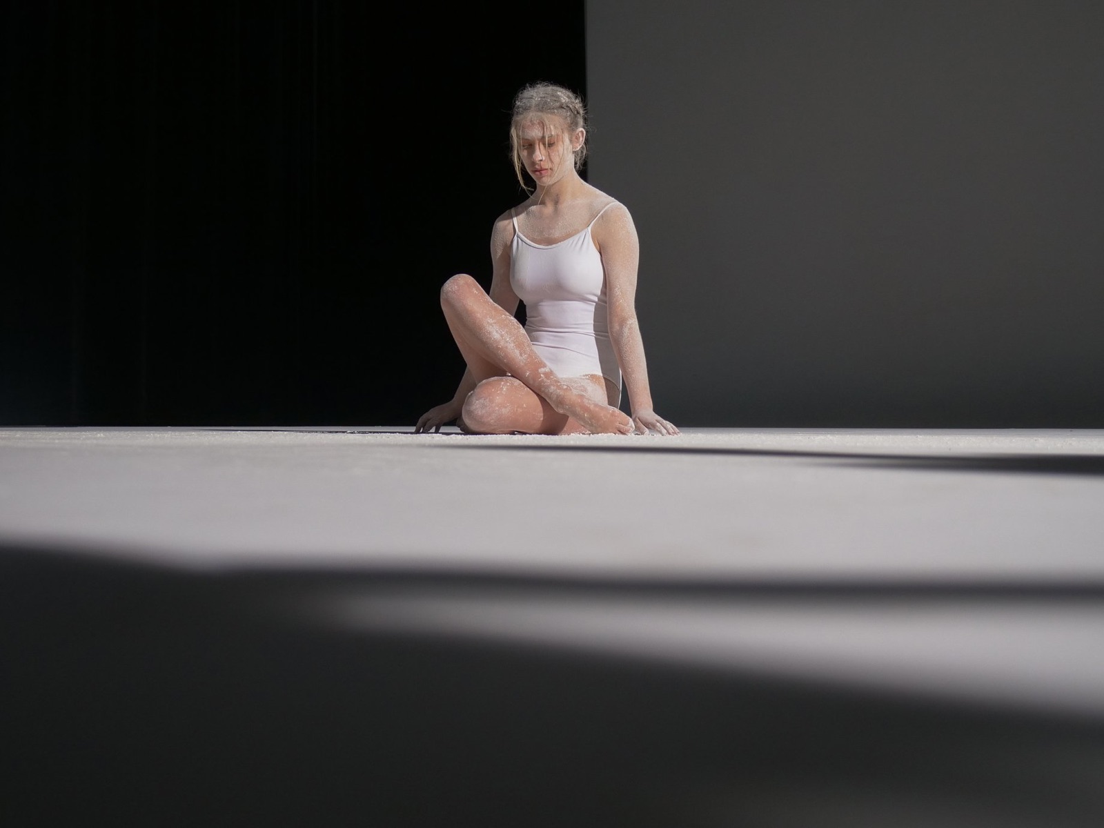 Dancer seated on a white floor cut by diagonal shadows
