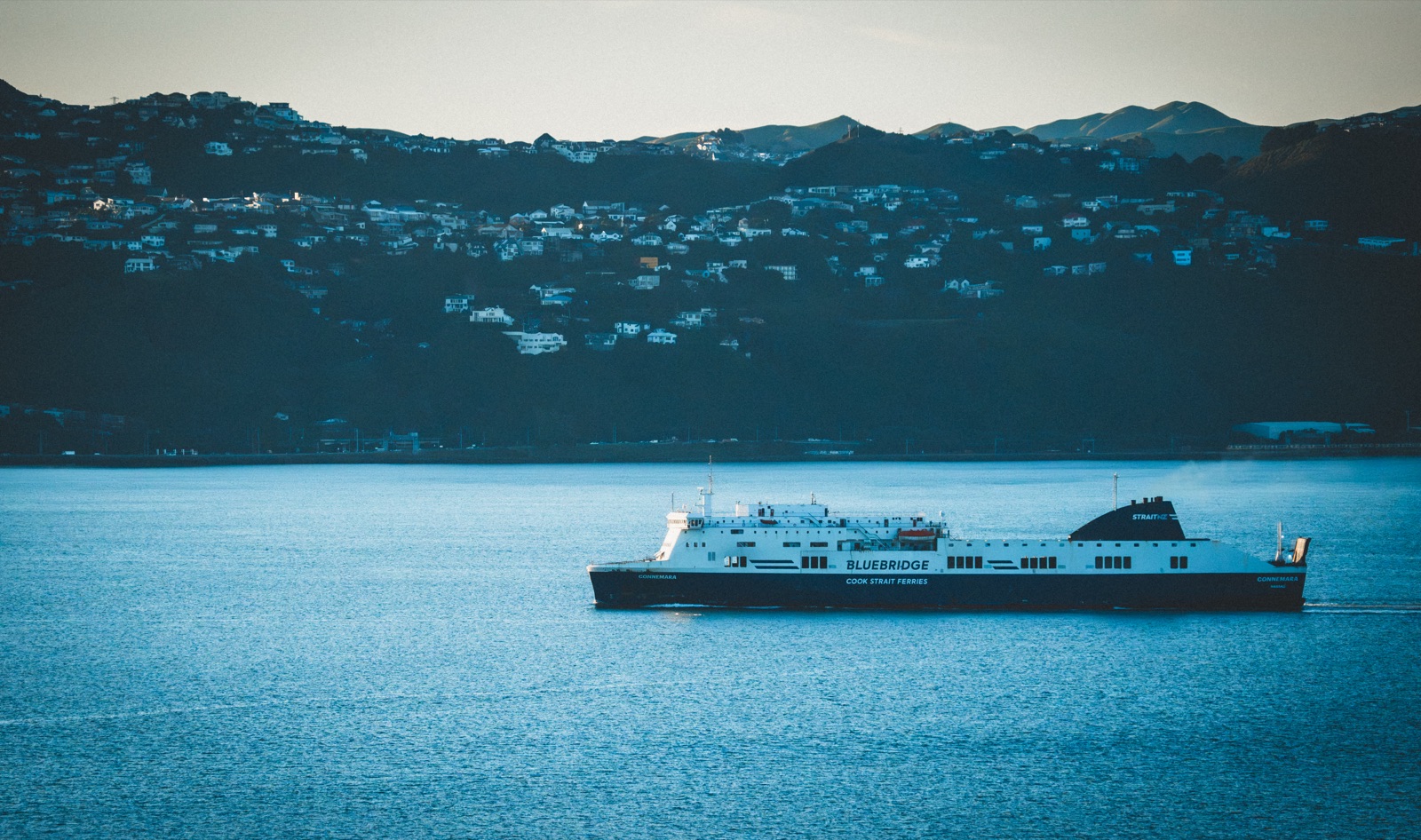 Ferry crossing a dark blue harbour at dusk